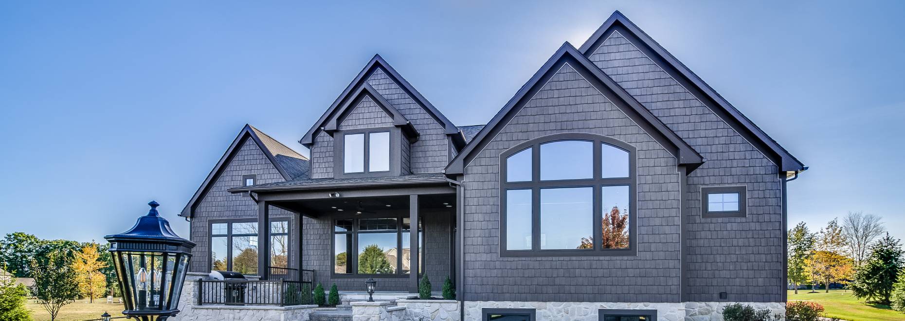 Modern gray brick house with large windows and sharp rooflines under a clear sky.