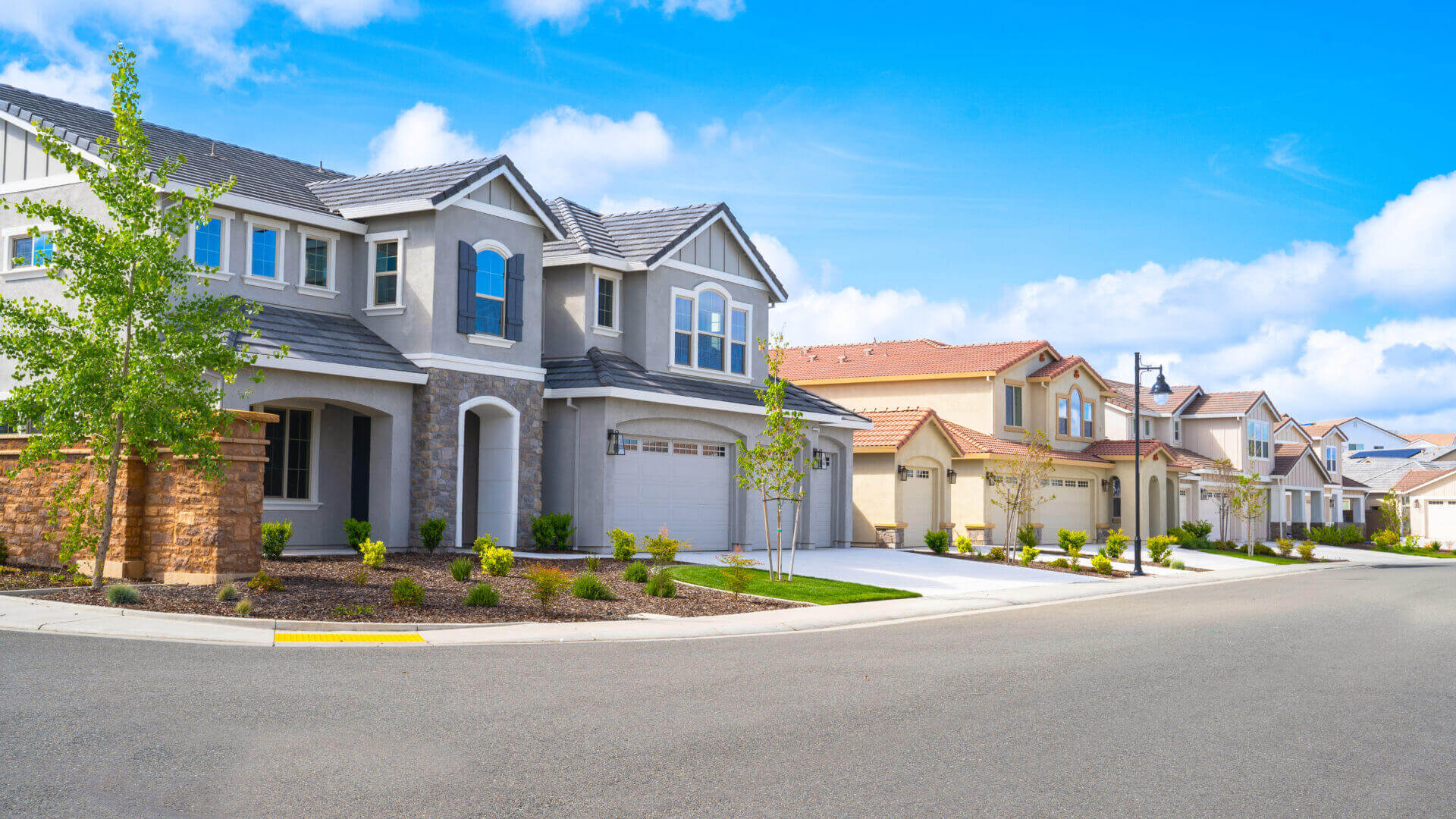 Row of modern suburban houses with well-kept lawns on a sunny day.