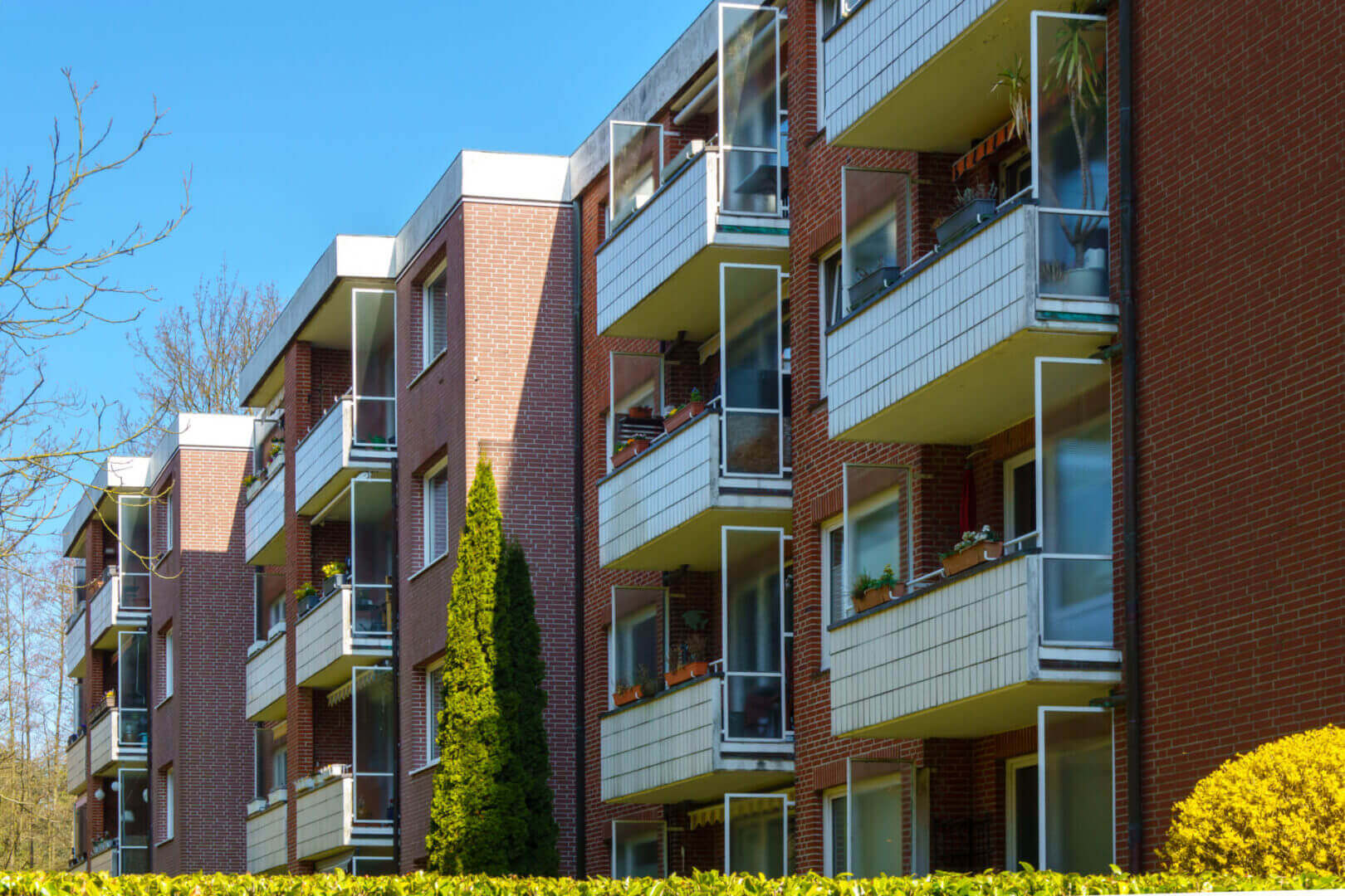 Modern apartment building with balconies and greenery on a sunny day.