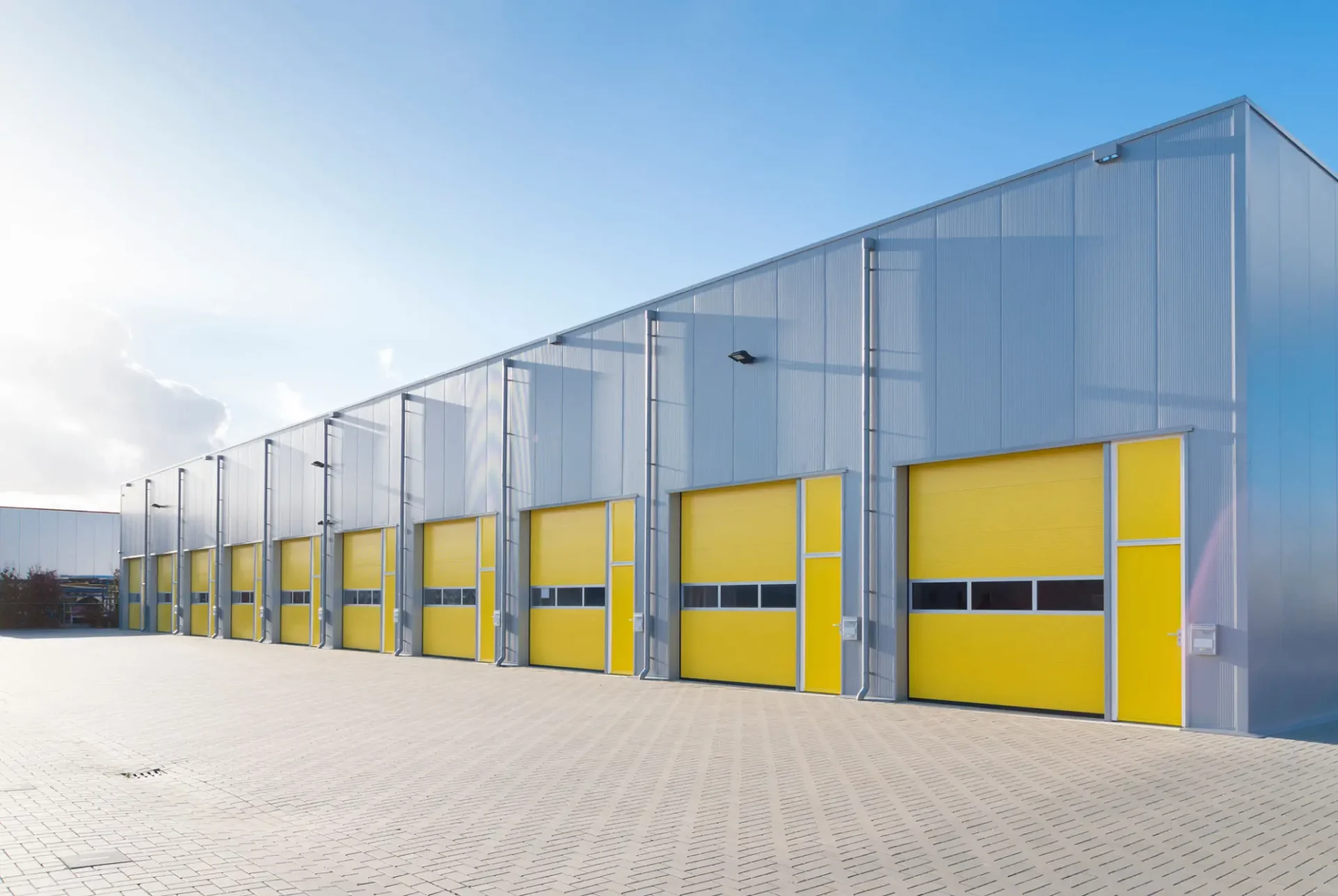 Modern industrial warehouse with yellow loading dock doors under a clear sky.